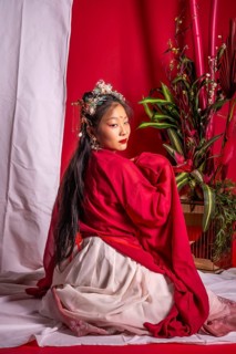 A woman in a red and white dress sits on a white surface. The woman is posing for a photo, and the