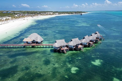 Aerial view of luxury overwater bungalows with thatched roofs and a wooden pier surrounded by