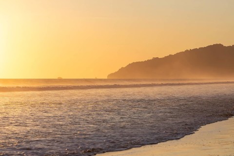 The low sun's golden light illuminates the ocean spray on Carate Beach, with views of Corcovado NP