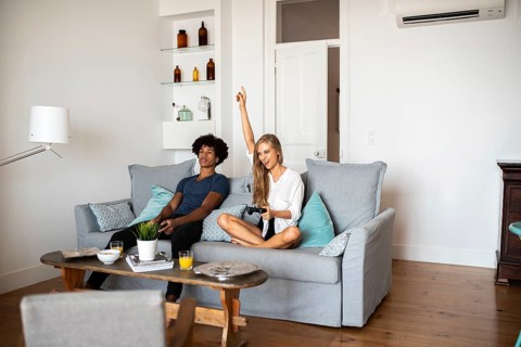 Two friends share a moment on a comfortable sofa while playing a video game. One raises a hand in