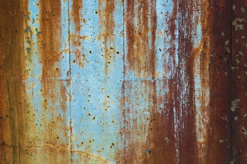 Close-up of long brownish rust streaks, stains and small holes on old light bluish painted concrete