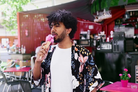 A man enjoys a refreshing ice cream cone on a warm summer day, standing in a vibrant outdoor