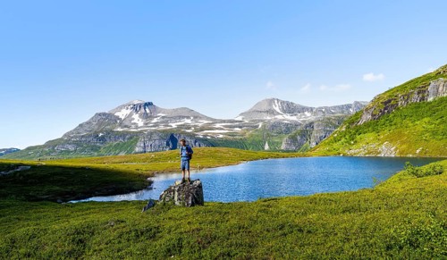 Hiker standing on a rock in front of a mountain landscape, small lake in the Flatvaddalen high