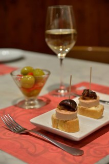 Foie gras with caramelized pumpkin on white bread, green olives, and white wine in a tapas bar,