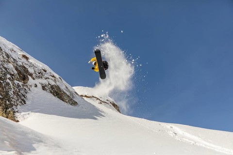 Thrilling image of a snowboarder executing a jump in the backcountry, surrounded by pristine