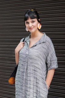 A young woman stands confidently against a textured wall wearing an oversized gray shirt and