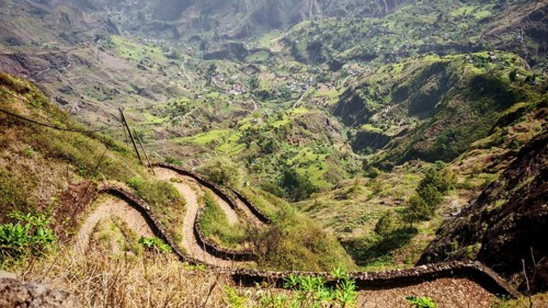 Curvy hiking trail, serpentines lead through a green landscape into a deep valley with surrounding