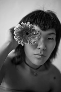 Black and white portrait of an Asian woman holding a flower to her eye, highlighting her serene and