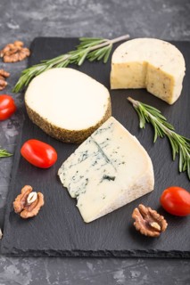 Blue cheese and various types of cheese with rosemary and tomatoes on black slate board on a black