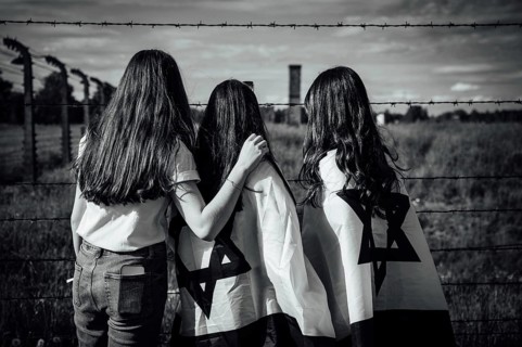 Jewish girls with Israeli flags by the fence of the concentration camp