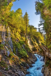 A sparkling waterfall in a sunlit gorge with a wooden bridge, Wimbachklamm gorge