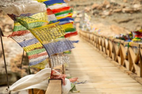 Vibrant prayer flags flutter on a wooden bridge near Phugtal Gompa in Ladakh, India. This serene