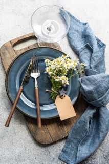 Top view of a rustic table setting with chamomile bouquet tied to a blue plate. Fork and knife are