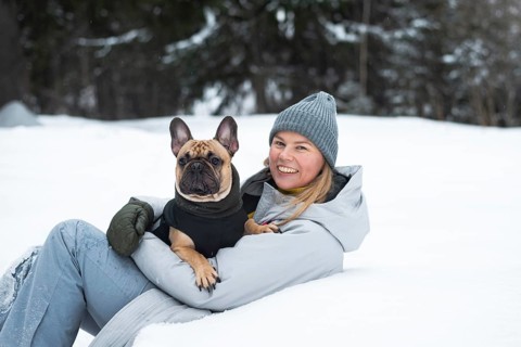 A cheerful person enjoys a winter day playing in the snow with a cute dog. Dressed warmly, they sit