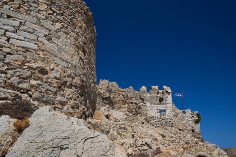 Historic stone wall with Greek flag, typical of Greece, under a clear blue sky, Johanniter Fortress