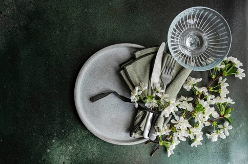 Aerial view of an elegant table setting with white blossoms, a glass, and cutlery on a ceramic