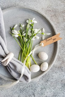 Top view of fresh snowdrops and speckled eggs arranged in a concrete dish, accompanied by a Thank