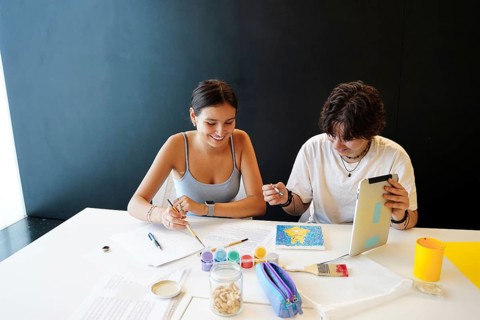 Two teenagers, one non-binary and one female, participate in artistic activities at school. They