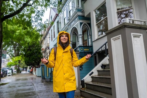 Woman in a vibrant yellow raincoat and backpack standing on a city sidewalk in san francisco,