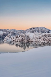 Dawn and sunrise at the wintry Forggensee in a snow-covered winter landscape in the foothills of