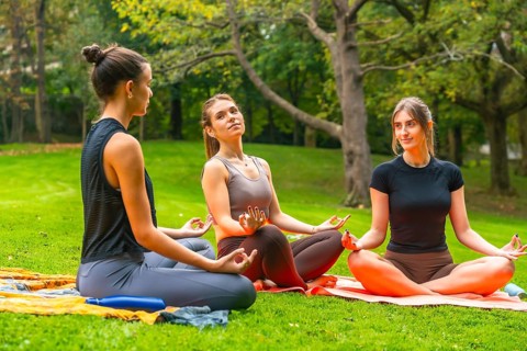 Three young women sitting in a park doing yoga and meditation together, finding balance and