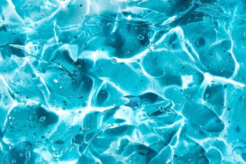 Close-up of a blue gel showcasing abstract fluid patterns and textures. The smooth surface reflects