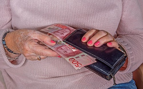 An elderly woman's hands take out Swedish banknotes from a wallet