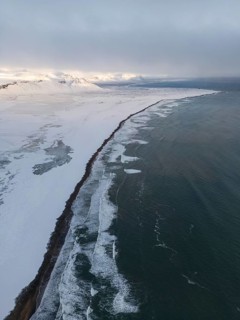 Aerial view of an Icelandic winter landscape, showcasing a stunning coastline with snow-covered