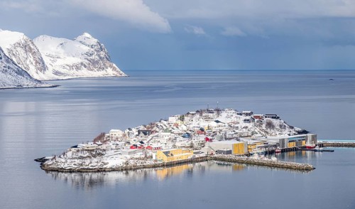 Aerial view of the snow-covered island of Husoy, Norway, surrounded by calm waters and rugged