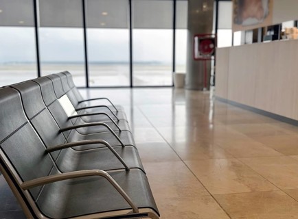 Empty airport seating area with metal benches, overlooking the tarmac through large windows. The