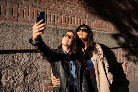 A multiethnic lesbian couple poses for a joyful outdoor selfie, exuding pride and love. The duo