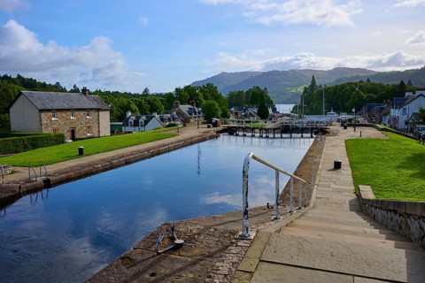 A paved canal area with views of buildings and mountains under clear skies, Caledonian Canal, Fort