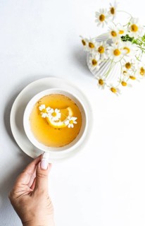 Top view of cropped unrecognizable woman's hand holding a cup of chamomile tea, garnished with