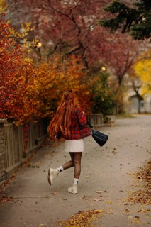 Back view of unrecognizable woman with red hair walking along a tree-lined path in Montreal. Fall