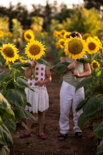 Two kids in a lush sunflower field hold large blooms covering their faces. The bright sunflowers