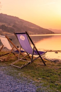 Sun loungers on the shore of a lake at sunset, surrounded by mountains and peaceful atmosphere,