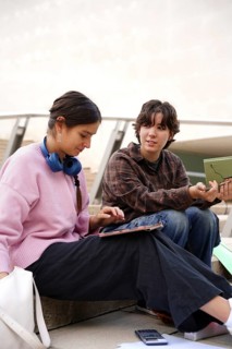 Two teenagers, a non-binary individual and a female, are seen engaging in educational activities