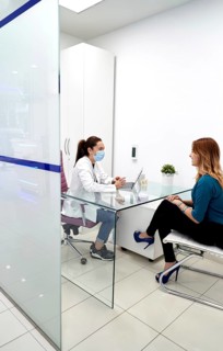 A dentist wearing a mask consults with a patient in a modern dental clinic. The setting features a