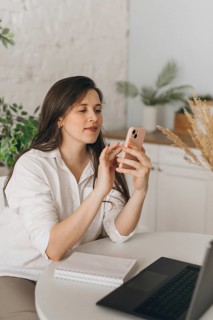 A nutritionist in a modern office setting uses her smartphone for virtual consultations. A laptop