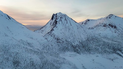 A breathtaking aerial view captures the majestic snow-covered mountains of a Nordic landscape,