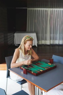 A woman thoughtfully engages in a game of backgammon at a table indoors The board's vibrant colors