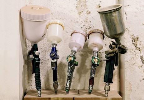 A collection of airbrushes and paint sprayers neatly arranged in a bass guitar luthier's workshop.
