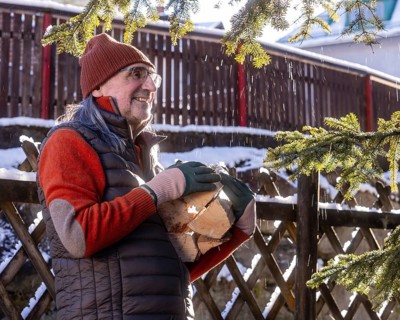 A senior man is wearing winter clothing and holding ecofirewood outdoors. He appears happy and