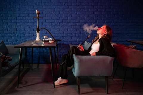 A young woman lounges comfortably in a modern hookah bar, enjoying a session. The space features a