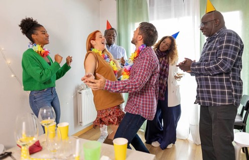 A lively birthday party with friends laughing and dancing, wearing colorful hats and leis. Glasses