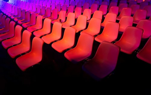 Rows of vibrant red chairs at a conference of AI in Amsterdam, illuminated by dynamic purple and