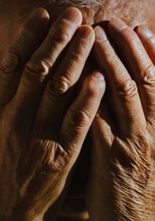 Close-up image of a senior man covering his face with both hands in deep thought The lighting