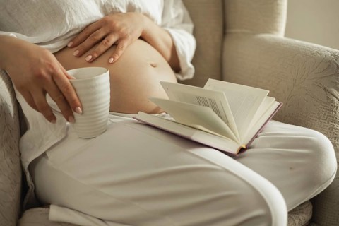 A serene scene of a pregnant woman relaxing in a cozy chair, with a book and a cup, symbolizing