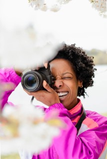 A joyful African American woman photographer, dressed in a colorful jacket, captures the beauty of