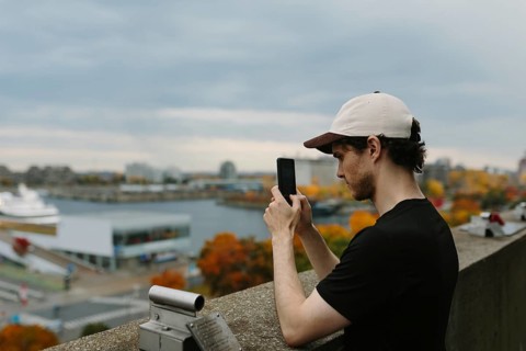 Side view of man in a cap captures a picturesque autumn view of Montreal with his phone, standing